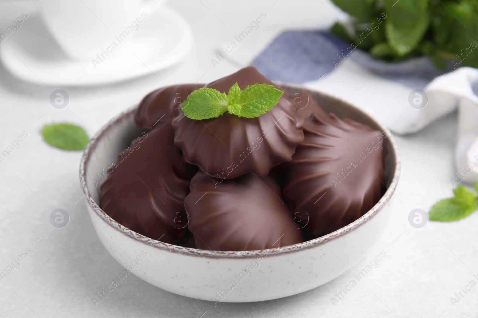 Photo of Delicious chocolate covered zephyrs with mint in bowl on white table, closeup