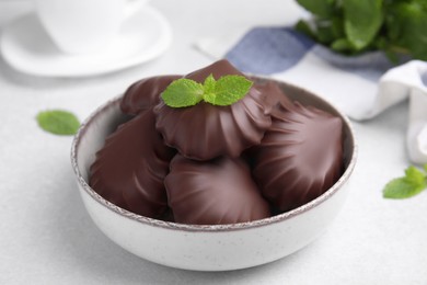 Delicious chocolate covered zephyrs with mint in bowl on white table, closeup