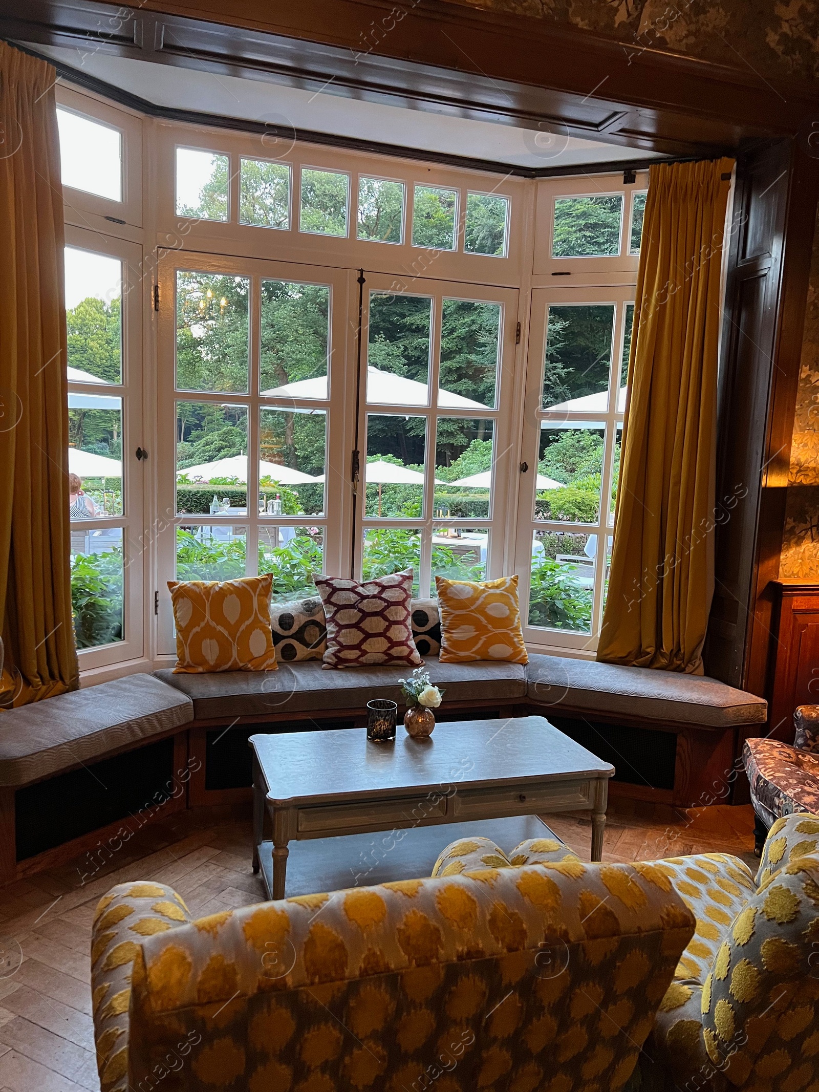 Photo of Wooden table near bay window seat with cushions in cozy room. Interior design