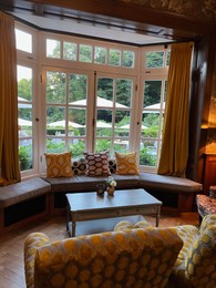 Photo of Wooden table near bay window seat with cushions in cozy room. Interior design