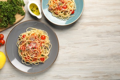 Delicious pasta with anchovies, tomatoes and parmesan cheese served on white wooden table, flat lay. Space for text