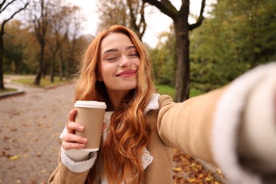 Photo of Portrait of beautiful woman with paper cup taking selfie in autumn park
