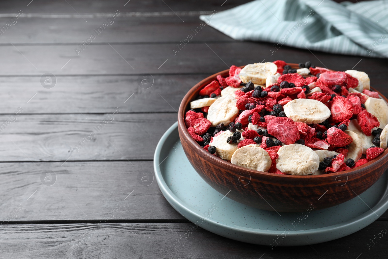 Photo of Bowl of different freeze dried fruits on wooden table. Space for text