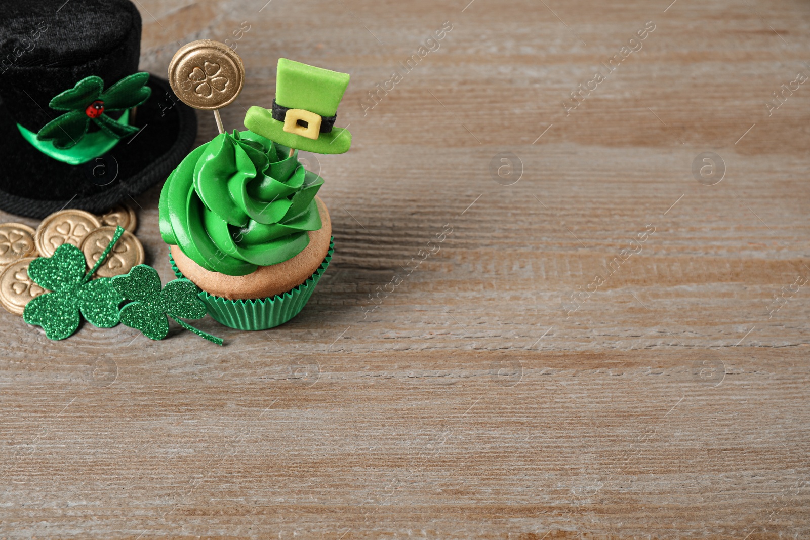 Photo of Decorated cupcake and hat on wooden table, space for text. St. Patrick's Day celebration