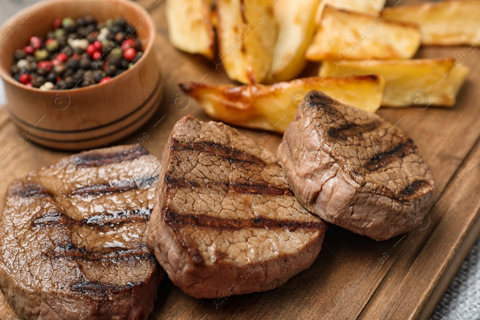 Photo of Grilled meat served with garnish on wooden board, closeup