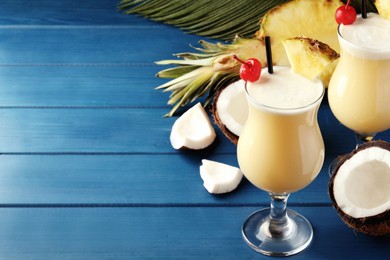 Photo of Tasty Pina Colada cocktails and ingredients on blue wooden table, space for text