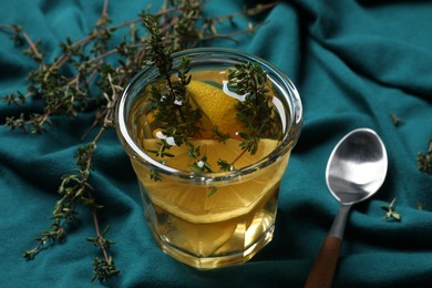 Glass of aromatic herbal tea with thyme and lemon on teal fabric