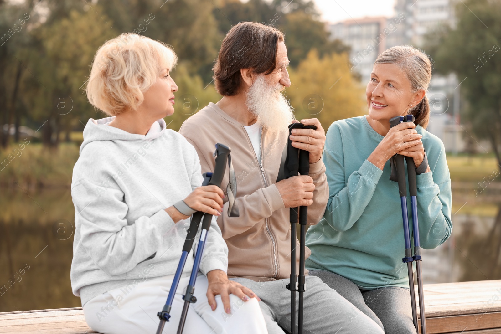 Photo of Group of senior people with Nordic walking poles sitting on wooden parapet outdoors