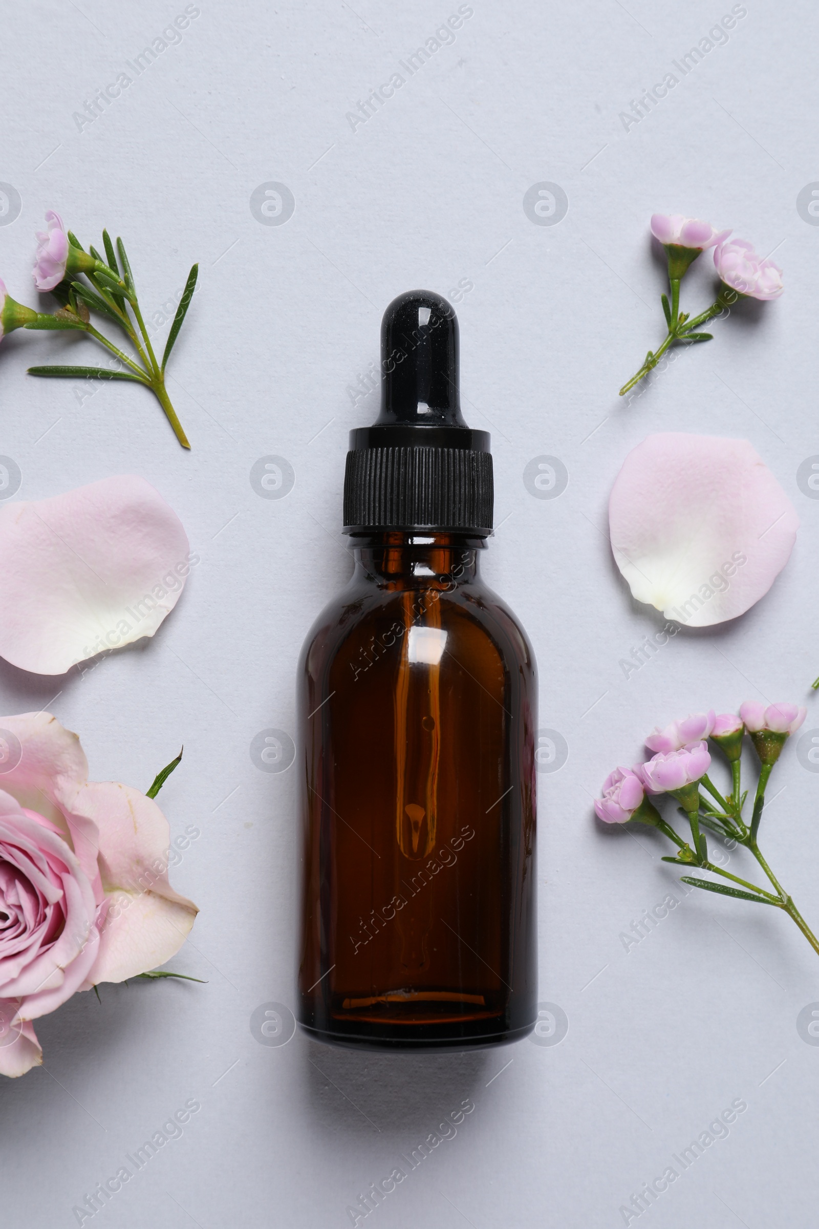 Photo of Bottle of cosmetic serum and beautiful flowers on light grey background, flat lay