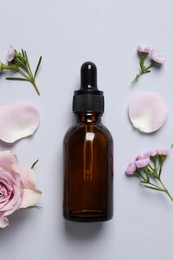 Bottle of cosmetic serum and beautiful flowers on light grey background, flat lay