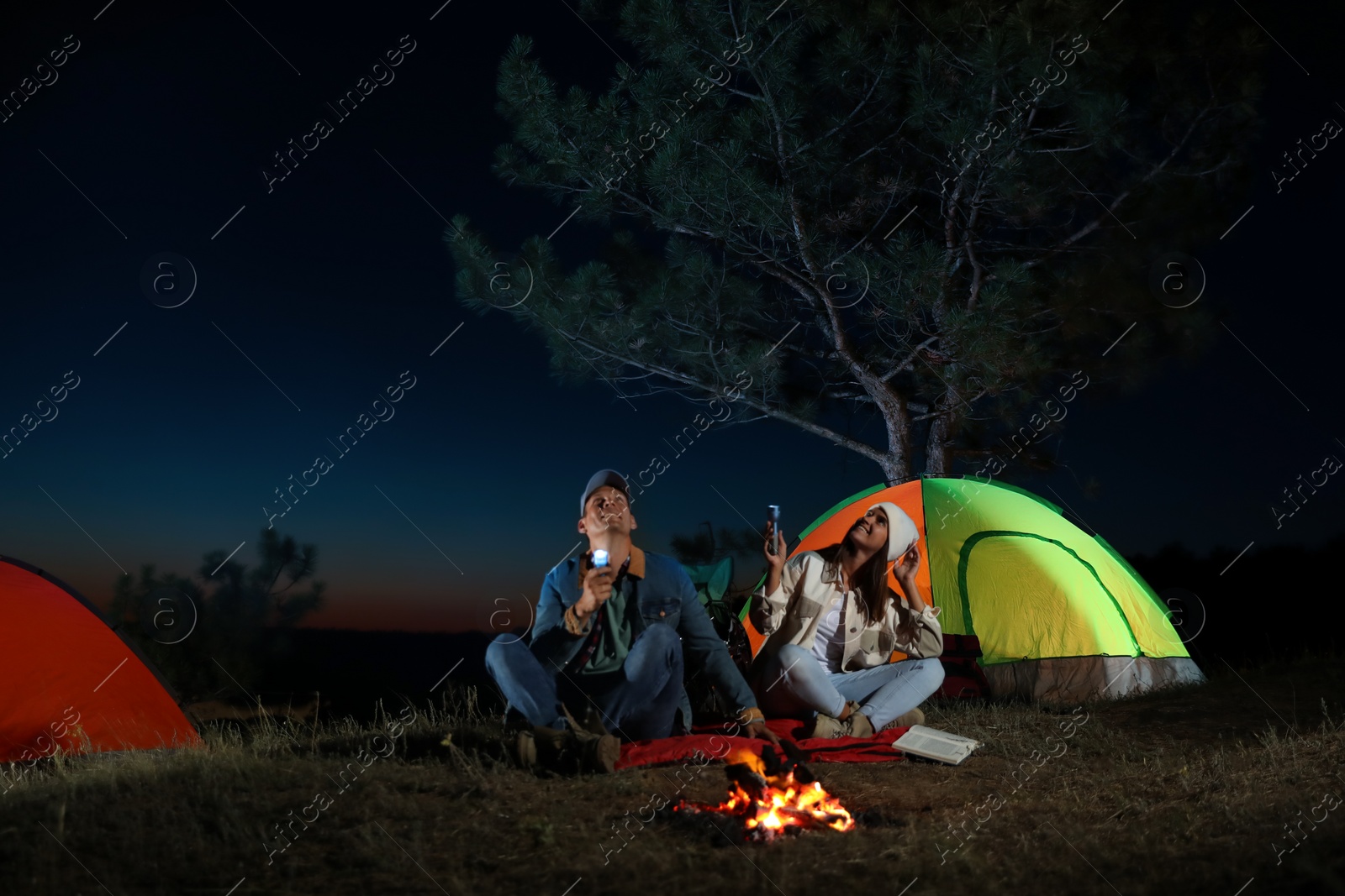 Photo of Couple with flashlights near bonfire at night. Camping season