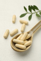 Photo of Vitamin capsules in spoon and leaves on white wooden table, closeup