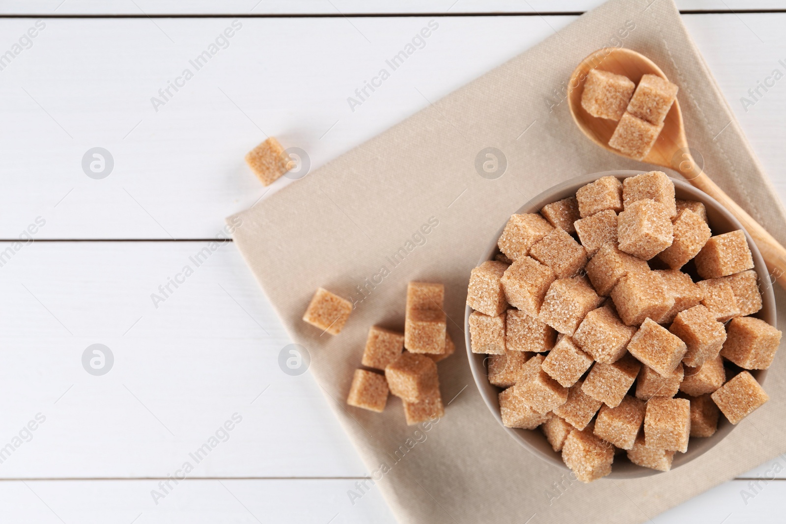 Photo of Brown sugar cubes on white wooden table, flat lay. Space for text