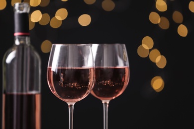 Glasses and bottle with delicious rose wine against blurred lights, closeup. Space for text