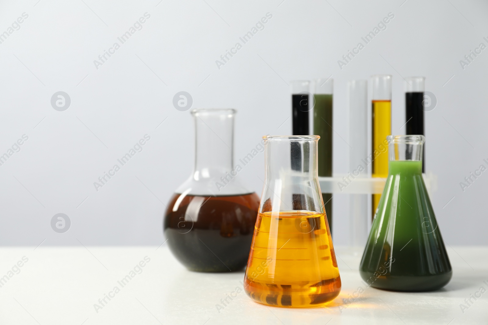 Photo of Laboratory glassware with different types of oil on white table, space for text