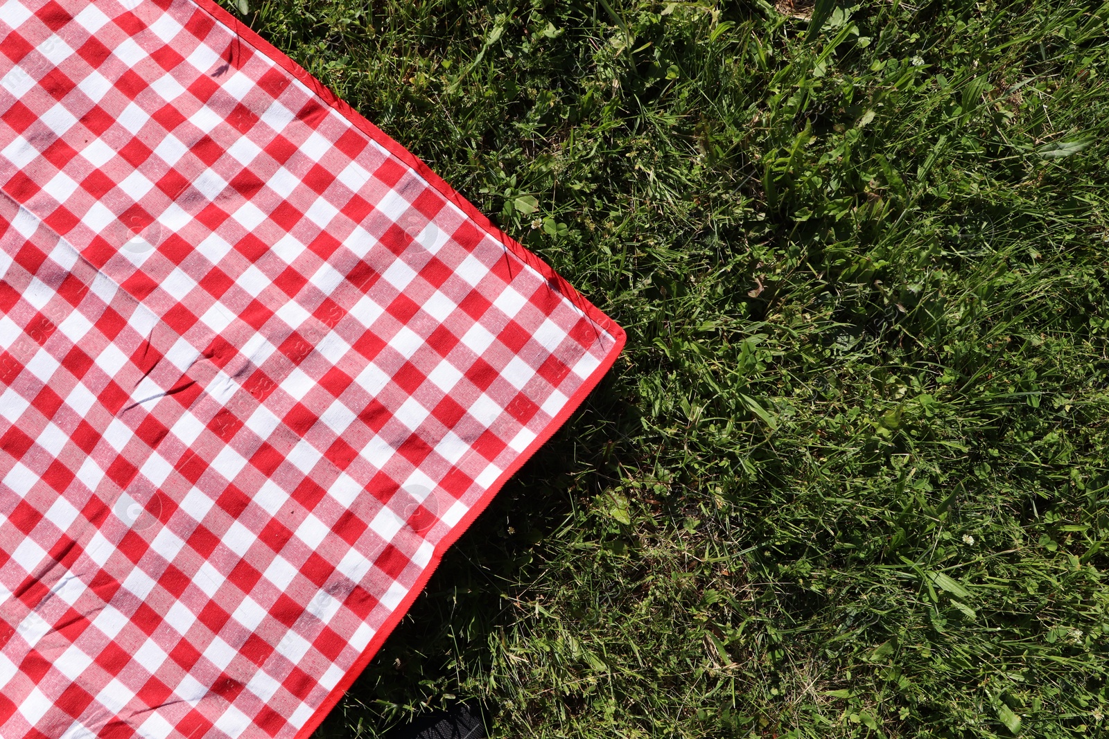 Photo of Checkered picnic tablecloth on fresh green grass, top view. Space for text