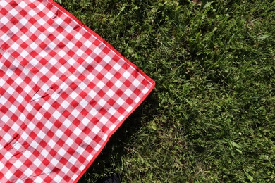 Checkered picnic tablecloth on fresh green grass, top view. Space for text