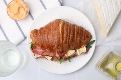 Photo of Tasty croissant with brie cheese, ham and bacon on white table, flat lay