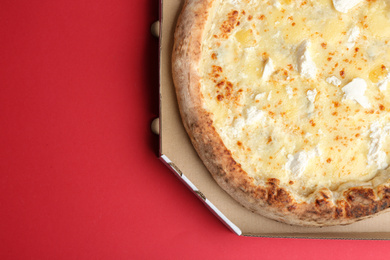 Photo of Delicious cheese pizza in takeout box on red background, top view