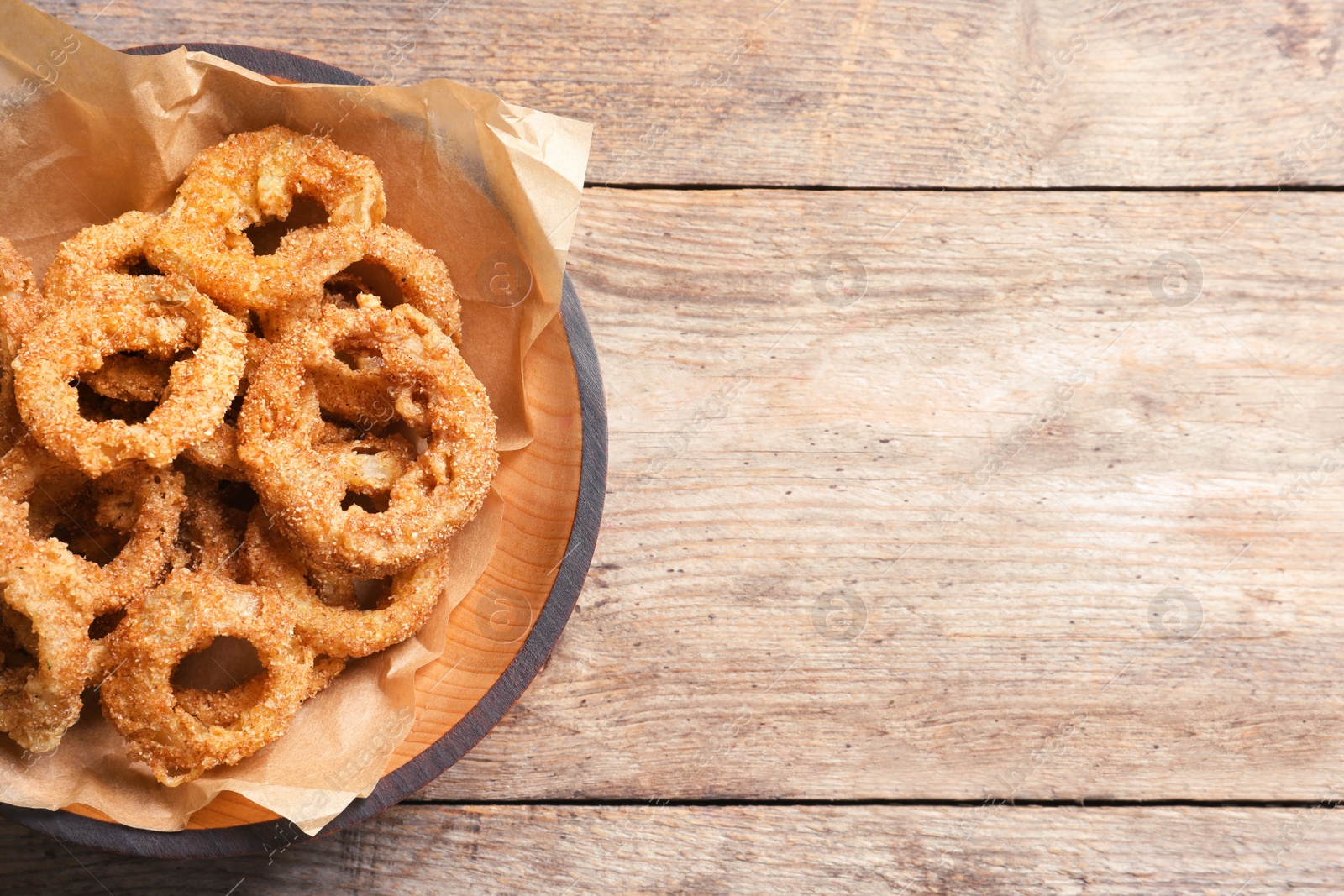 Photo of Homemade crunchy fried onion rings in plate on wooden background, top view. Space for text