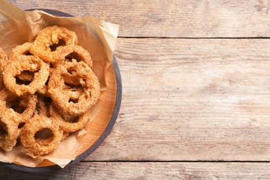 Homemade crunchy fried onion rings in plate on wooden background, top view. Space for text