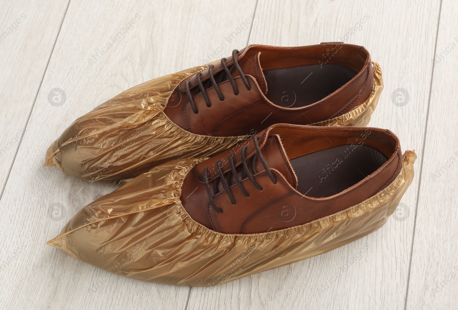 Photo of Men`s shoes in shoe covers on light wooden floor