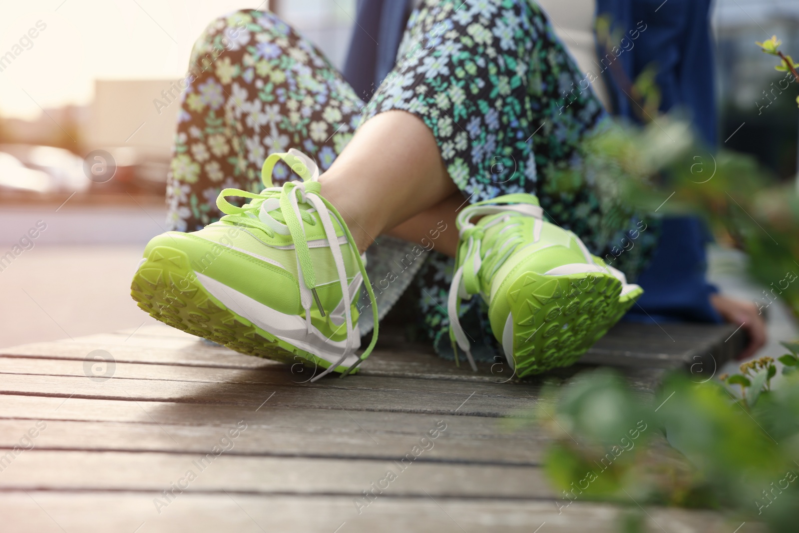 Photo of Woman in stylish sneakers sitting on wooden bench outdoors, closeup