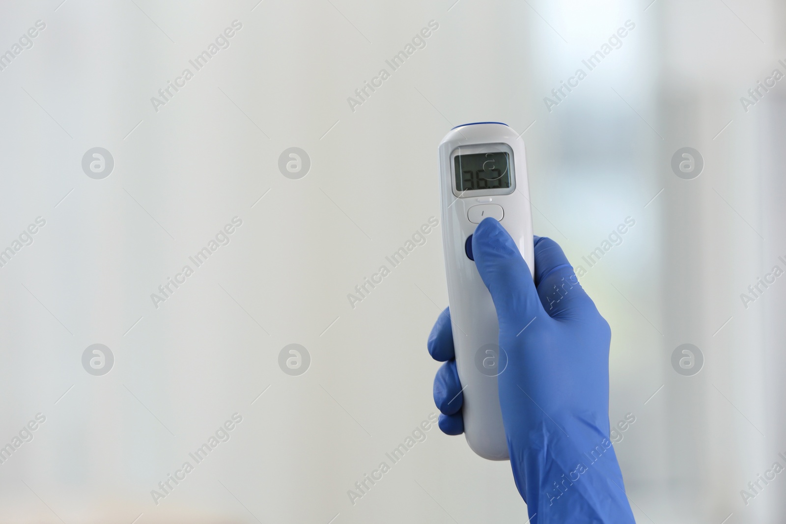 Photo of Closeup view of doctor with infrared thermometer on blurred background, space for text. Checking temperature during Covid-19 pandemic