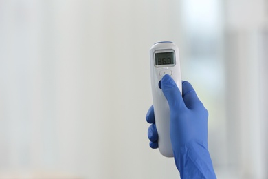 Photo of Closeup view of doctor with infrared thermometer on blurred background, space for text. Checking temperature during Covid-19 pandemic