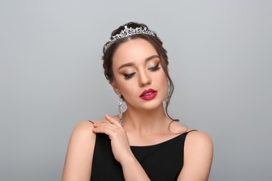 Beautiful young woman wearing luxurious tiara on light grey background