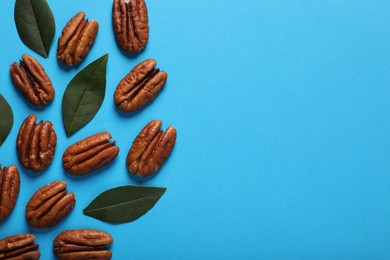 Delicious pecan nuts and green leaves on light blue background, flat lay. Space for text