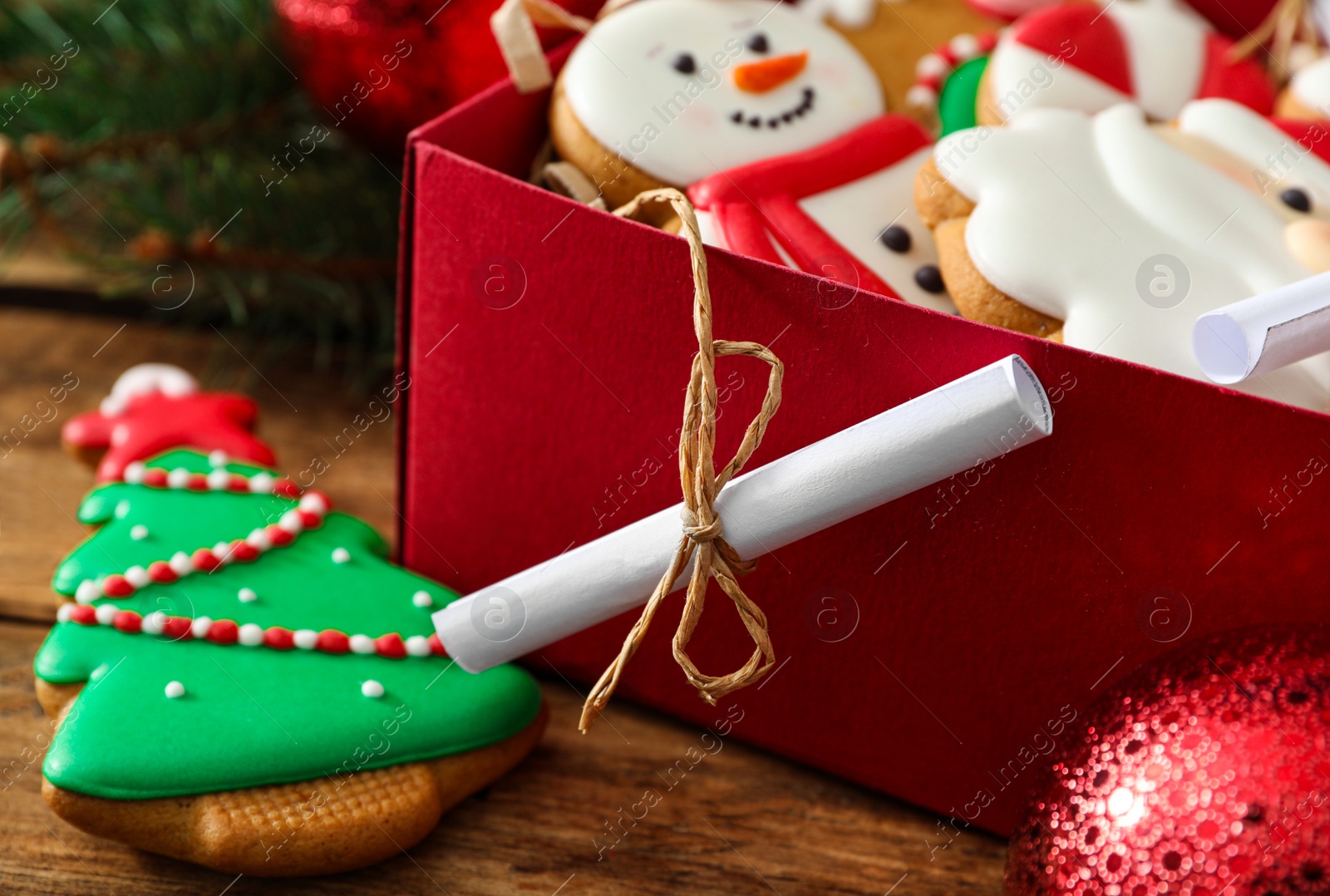 Photo of Rolled note near gift box with Christmas cookies on wooden table, closeup. Advent calendar