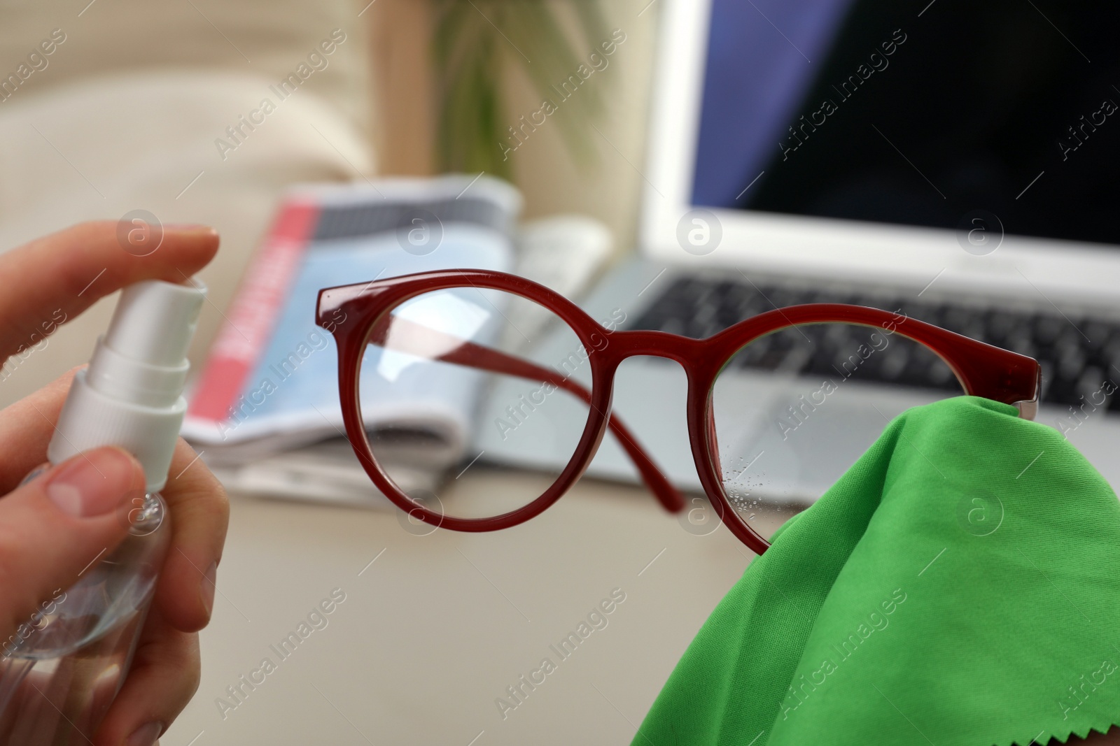 Photo of Woman cleaning glasses with microfiber cloth and spray at home, closeup