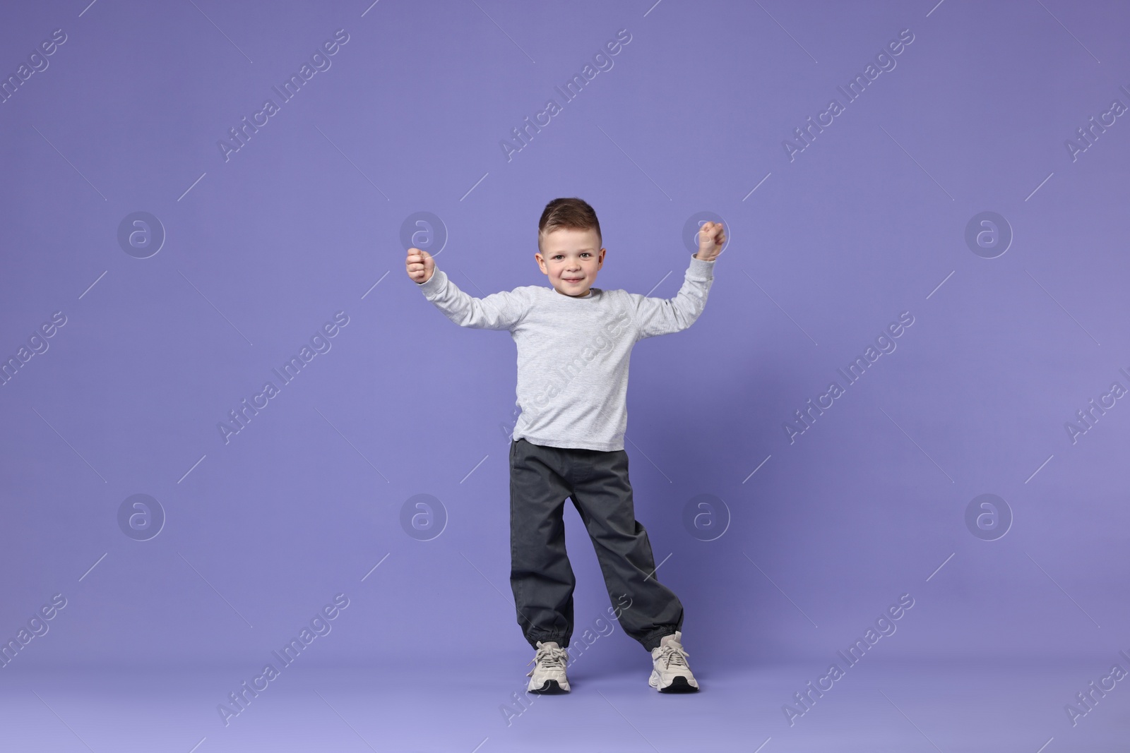 Photo of Happy little boy dancing on violet background