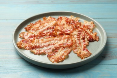 Photo of Delicious fried bacon slices on blue wooden table