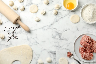 Photo of Flat lay composition with raw dumplings and ingredients on marble background, space for text. Process of cooking