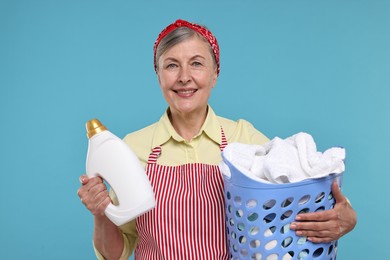 Happy housewife with detergent and basket full of laundry on light blue background