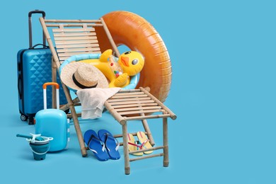 Photo of Deck chair, suitcases and beach accessories on light blue background, space for text. Summer vacation