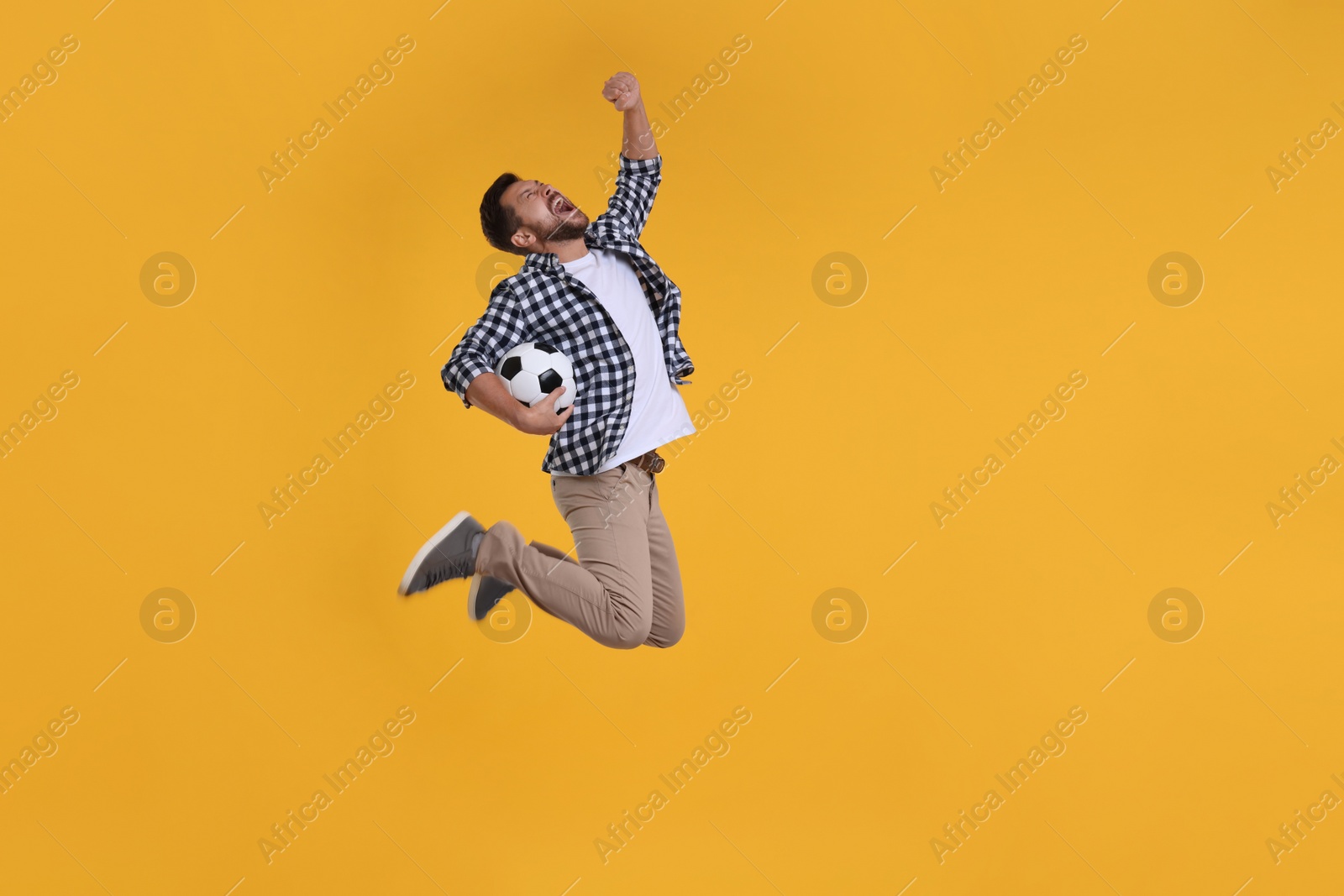 Photo of Emotional sports fan with ball jumping on yellow background. Space for text