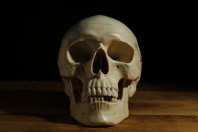 Photo of Human skull on wooden table against black background