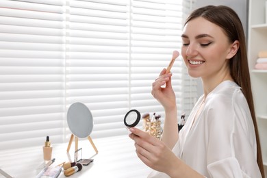 Photo of Beautiful young woman applying blusher with brush at dressing table indoors. Space for text