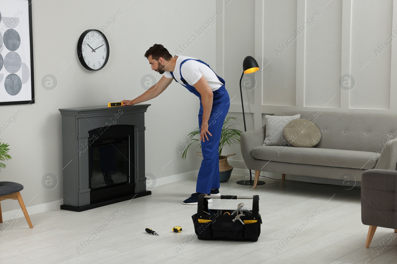 Photo of Professional technician using construction level for installing electric fireplace in room