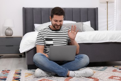 Photo of Happy man greeting someone during video chat via laptop in bedroom