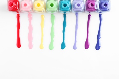 Photo of Spilled colorful nail polishes and bottles on white background, top view