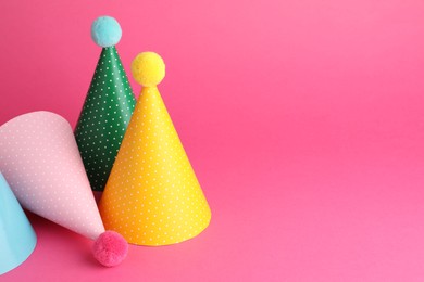 Photo of Beautiful party hats with pompoms on pink background, space for text