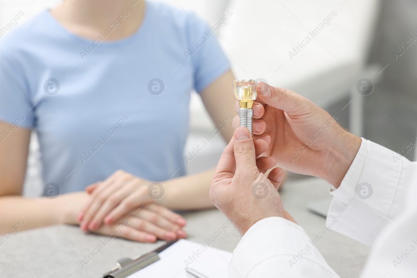 Photo of Doctor showing patient educational model of dental implant in clinic, closeup. Space for text