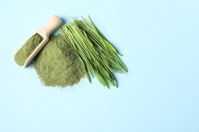 Photo of Pile of wheat grass powder, scoop and fresh sprouts on light blue table, flat lay. Space for text