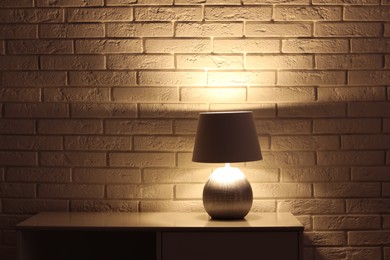 Photo of Stylish glowing night lamp on table near white brick wall. Space for text