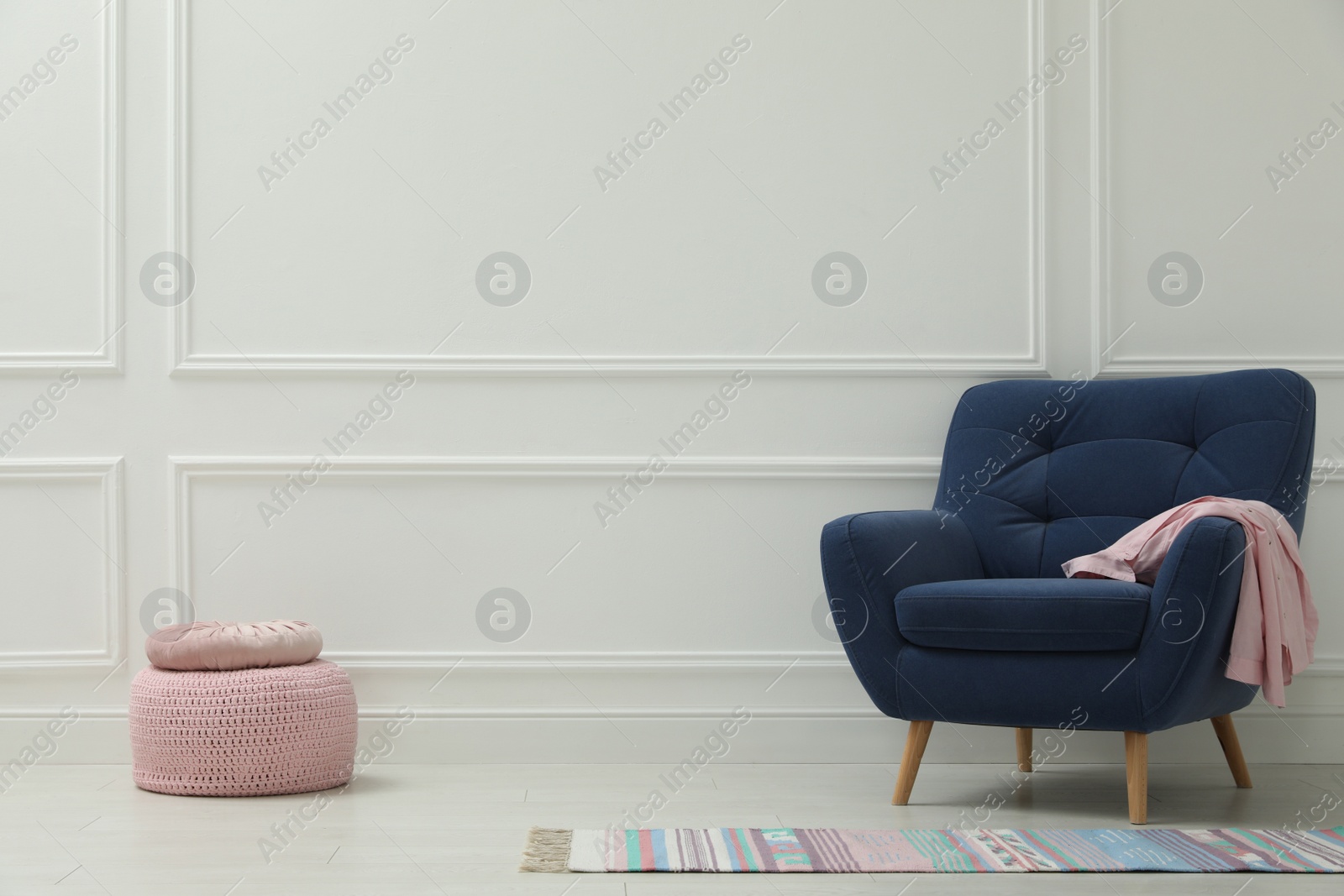 Photo of Stylish room interior with pouf, armchair and colorful rug. Space for text