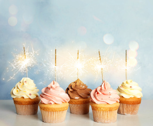 Image of Birthday cupcakes with sparklers on table against light blue background